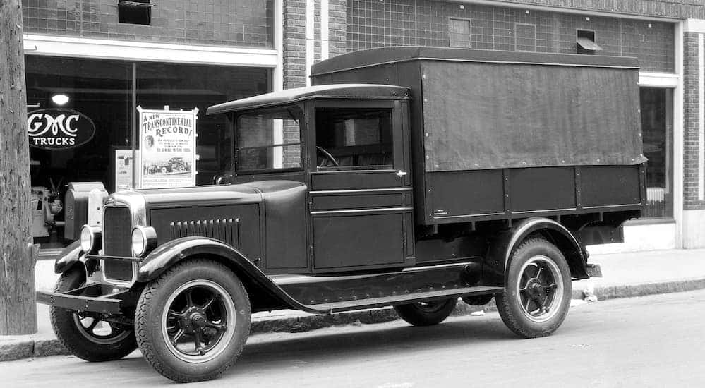 A black 1928 GMC T-11 Canopy Express, shown in black and white, is parked in front of a General Motors store.