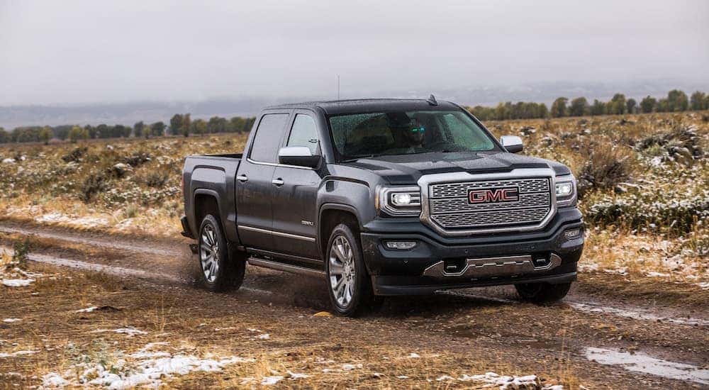 A blue 2018 GMC Sierra 1500, which is a popular option among used trucks, is driving on a muddy dirt road near Atlanta, GA.