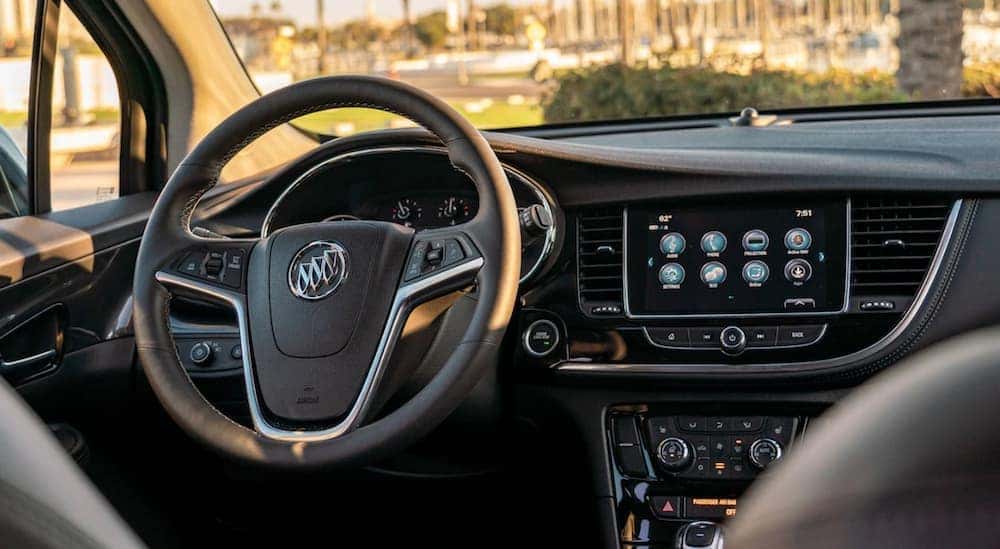 The front black interior of a 2020 Buick Encore is shown with an infotainment system and drivers display.