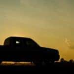 A group of friends are in the bed of their pickup truck while watching the springtime sun set.