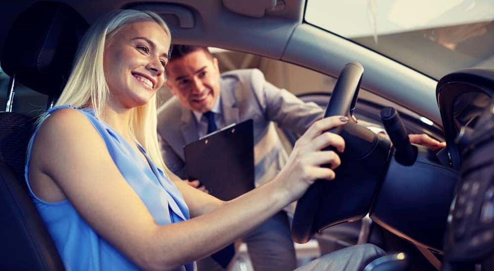 A smiling woman is test driving a used truck.