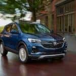 A blue 2020 Buick Encore GX is driving past brick building near Atlanta, GA.