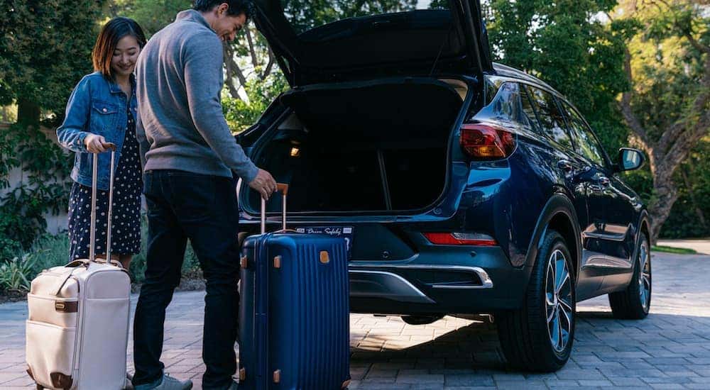 A couple is loading suitcases into the back of a blue 2020 Buick Encore GX.