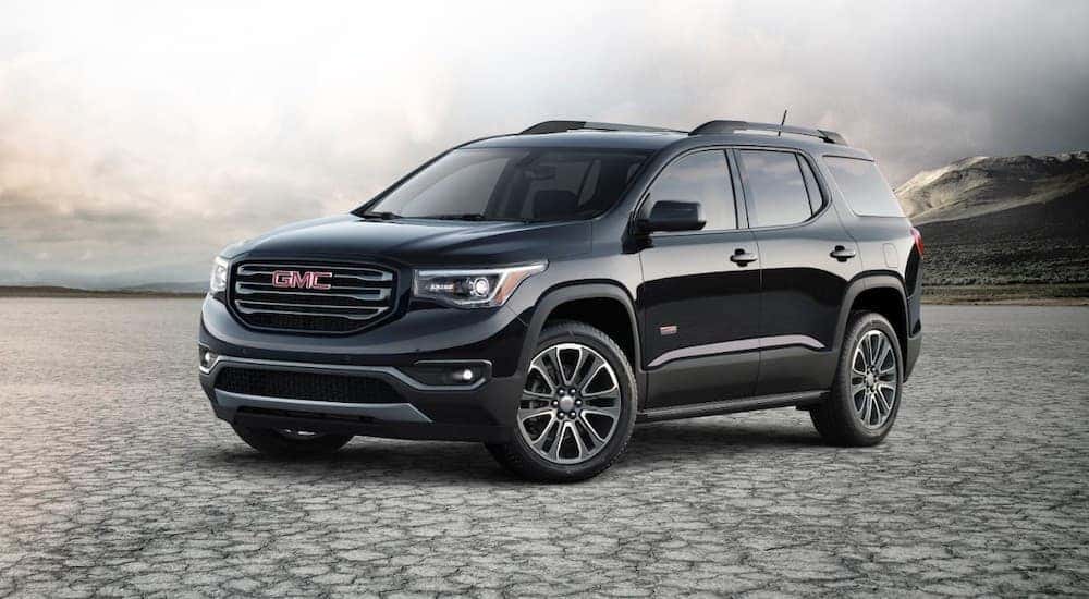 A black 2017 GMC Acadia is parked in a salt flat in front of mountains.