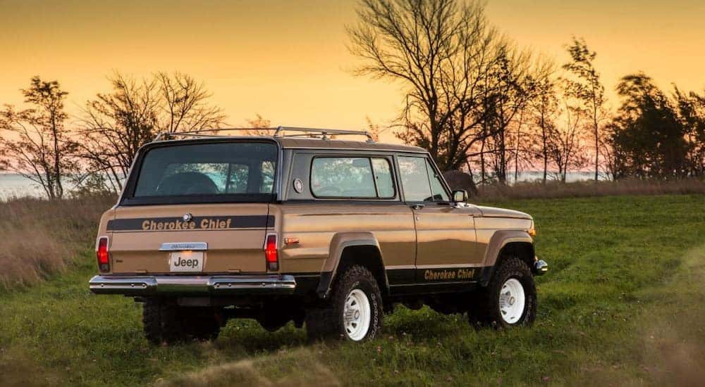 A tan 1977 Jeep Cherokee Chief is parked off-road at sunset.