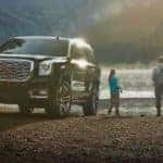 A black 2020 GMC Yukon, the largest of the GMC SUVs, is parked next to a couple fishing at a lake.