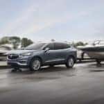 One of the most popular used SUVs for sale, a grey 2019 Buick Enclave, is shown towing a boat past a marina.