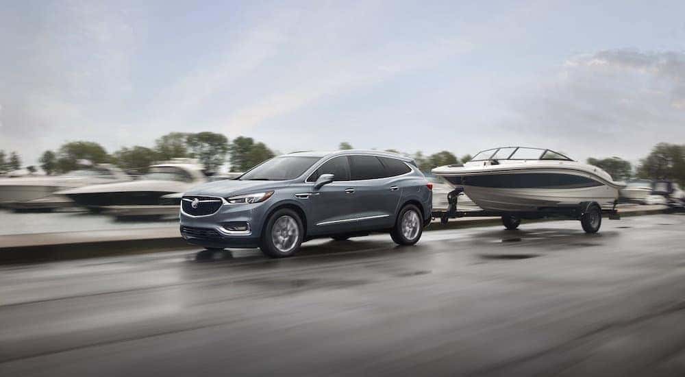 One of the most popular used SUVs for sale, a grey 2019 Buick Enclave, is shown towing a boat past a marina.