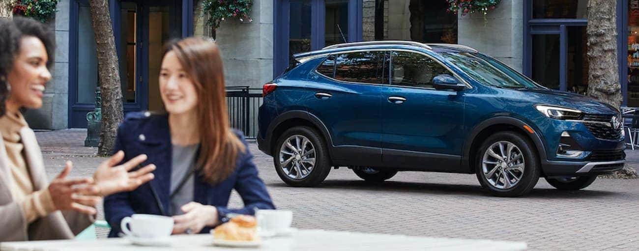 A blue 2020 Buick Encore GX is parked behind two women outside at a cafe after winning the 2020 Buick Encore GX vs 2020 BMW X1 comparison.