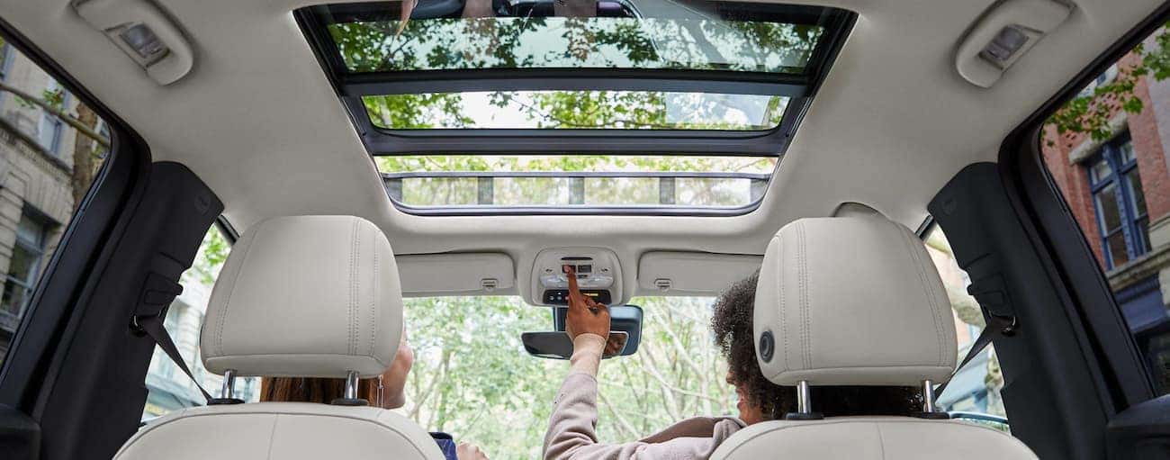 A passenger is opening the sunroof in the white interior of a 2020 Buick Encore GX.