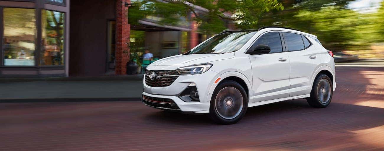 A white 2020 Buick Encore GX is driving around a corner past a brick building near Atlanta, GA.