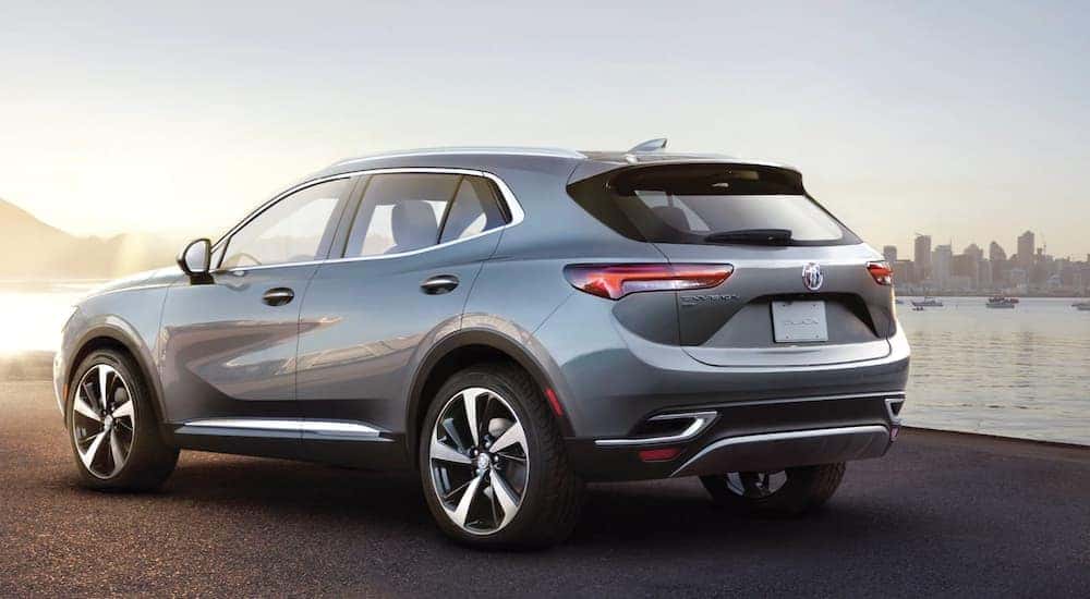 A grey 2021 Buick Envision is shown from the rear in front of a bay at sunset.