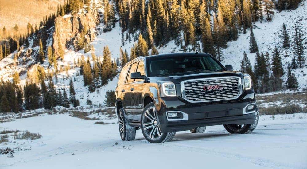 A black 2019 GMC Yukon Denali is driving on a snowy mountain road.