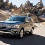 A gray 2018 Ford Expedition is driving on a highway past large rock formations.