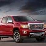 A red 2020 GMC Canyon Denali from a local GMC dealer is parked in front of a glass building at dusk.