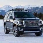 A black 2021 GMC Yukon Denali from a local GMC dealer is parked on a snowy field in front of snow-covered mountains.