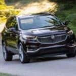 A black 2018 used Buick Enclave Avenir is driving on a tree-lined road.