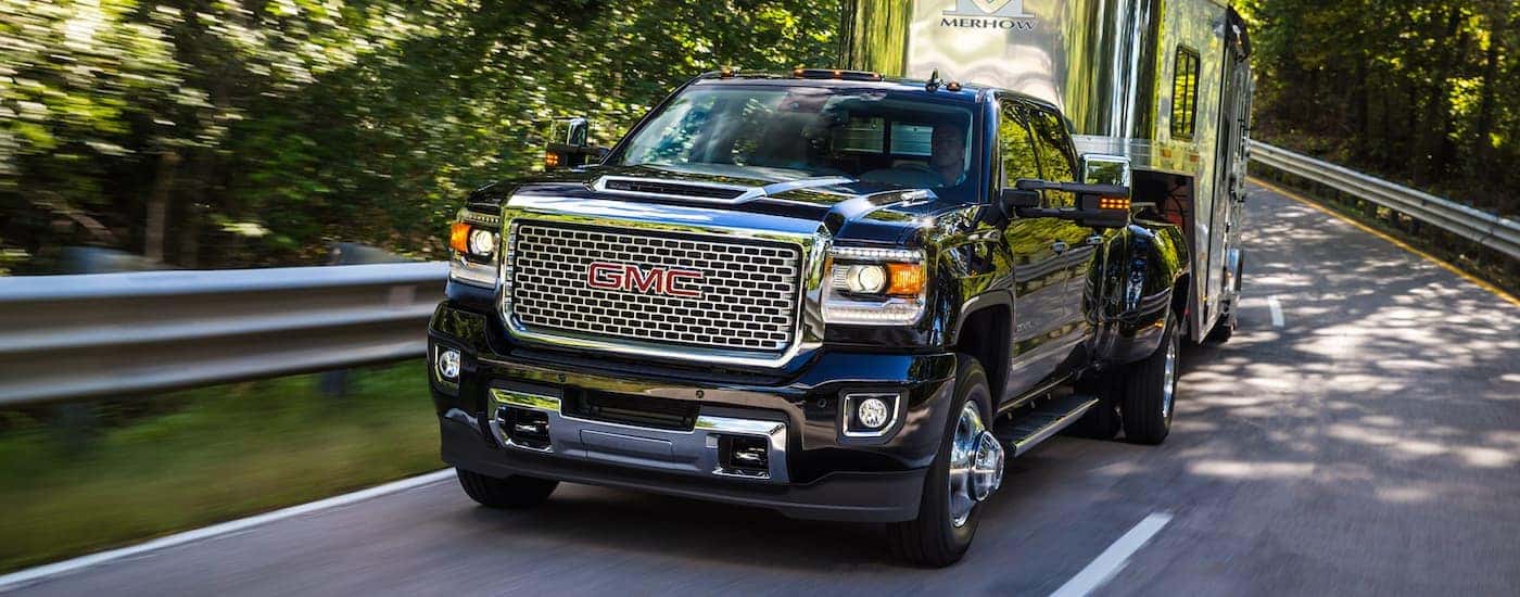 A black 2017 Used GMC Sierra 3500 is towing an enclosed 5th wheel trailer on a tree-lined road.