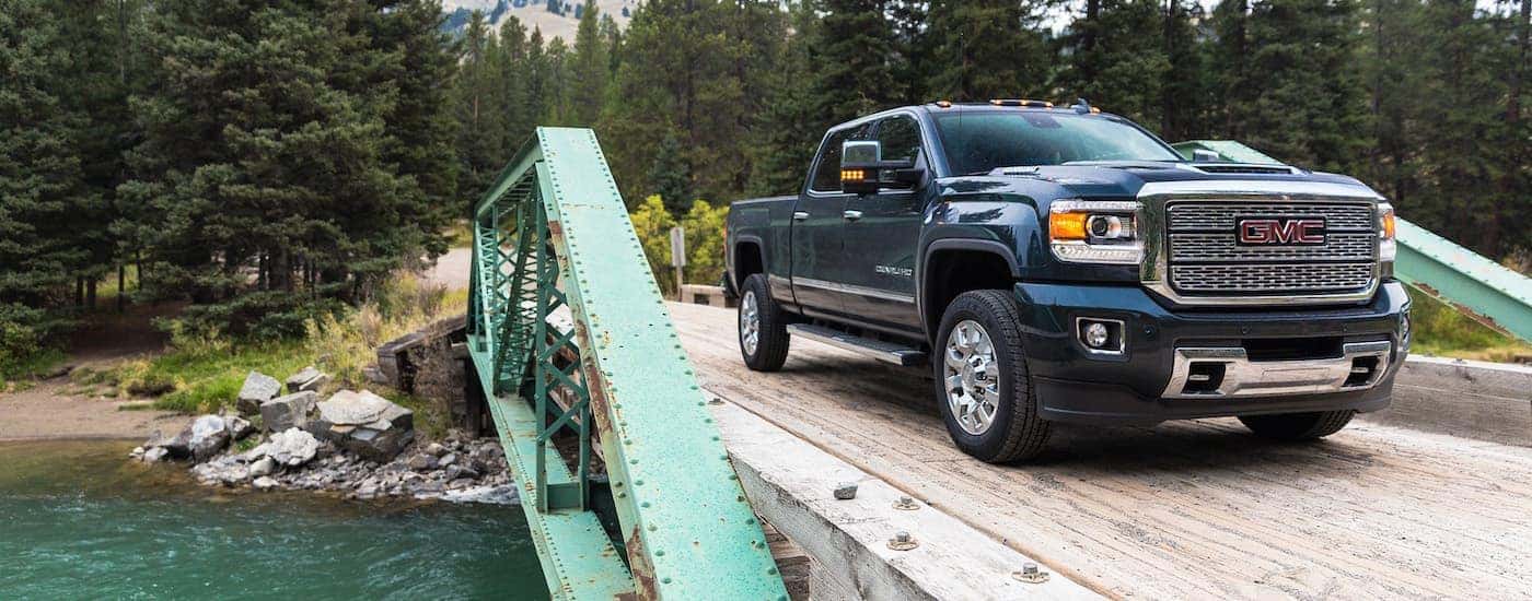 A blue 2018 Used GMC Sierra 2500 is driving on a green metal bridge over a river.
