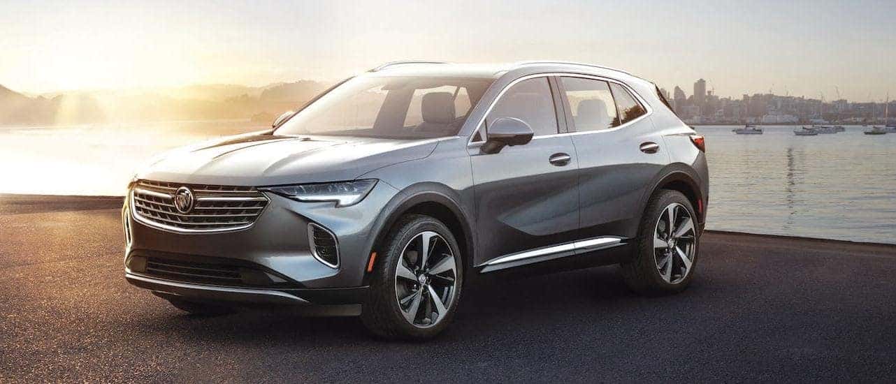 A silver 2021 Buick Envision is parked in front of a river and city.