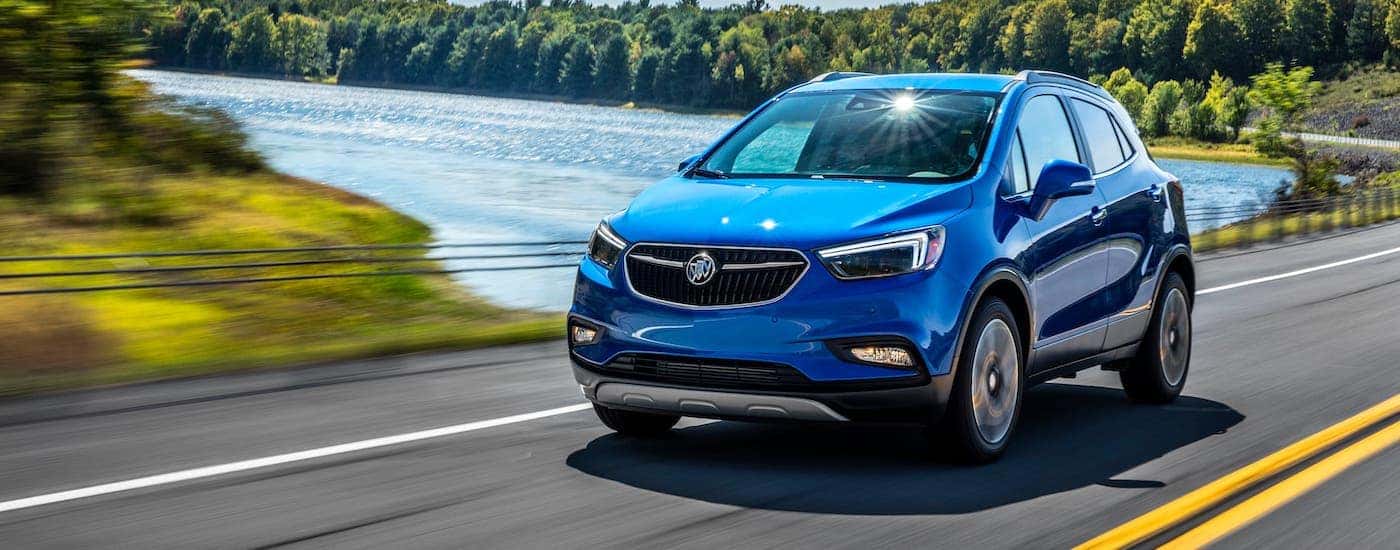 A blue 2020 Buick Encore is driving on a highway past a lake.