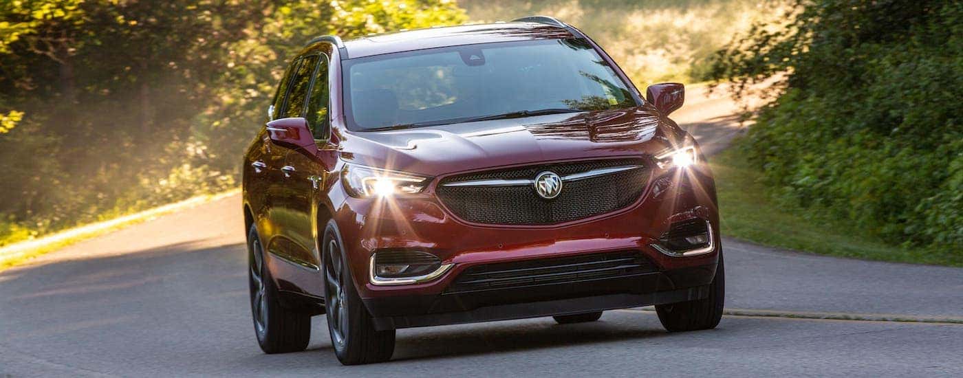 A red 2020 Buick Enclave SportTouring is driving on a tree-lined road.