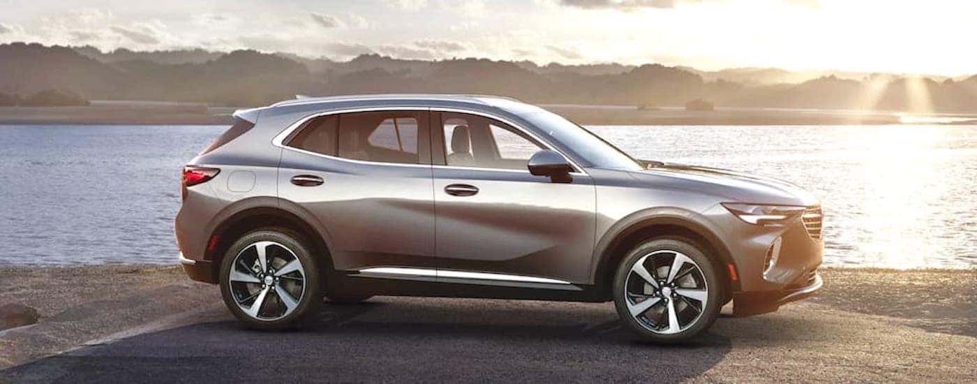A silver 2021 Buick Envision is shown from the side parked in front of a river at sunset.