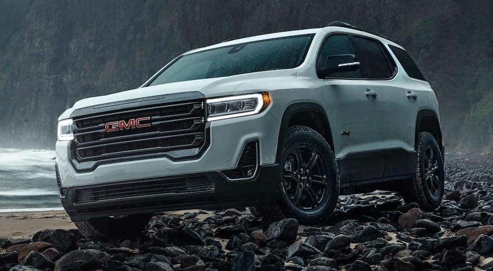 A white 2021 GMC Acadia is off-roading on rocks in the rain.