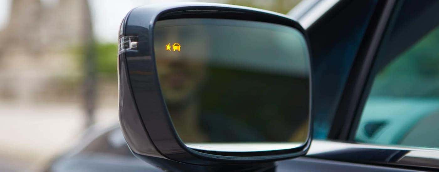 A close up shows the illuminated blind spot indicator on the side mirror of a dark grey 2021 Buick Enclave.