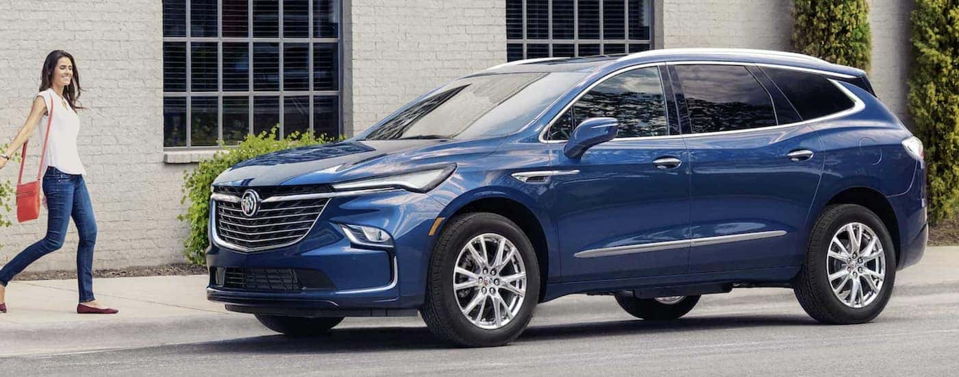A blue 2023 Buick Enclave is shown from the side parked in front of a city building.