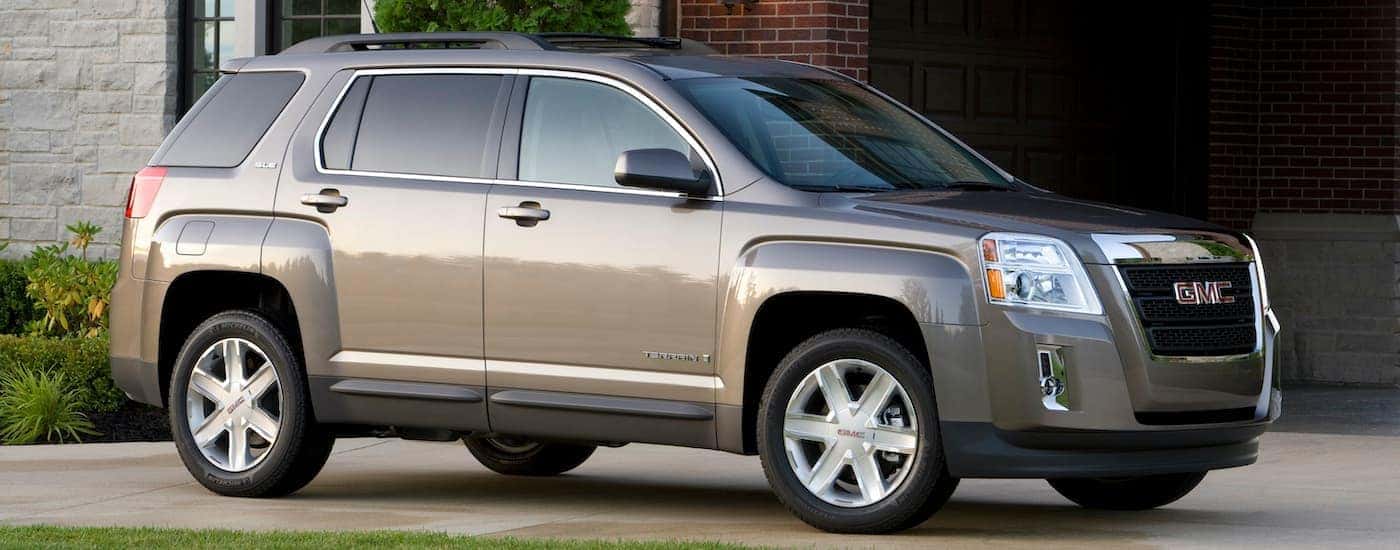 A tan 2010 GMC Terrain is shown from the side parked in front of a house.