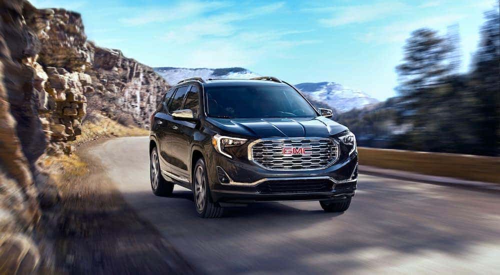 A black 2020 GMC Terrain Denali, from a used GMC Terrain dealer, is shown driving down a road past a rock face.
