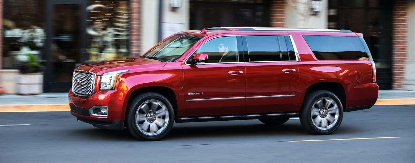 A red 2017 GMC Yukon Denali XL is shown from the side driving through a city.