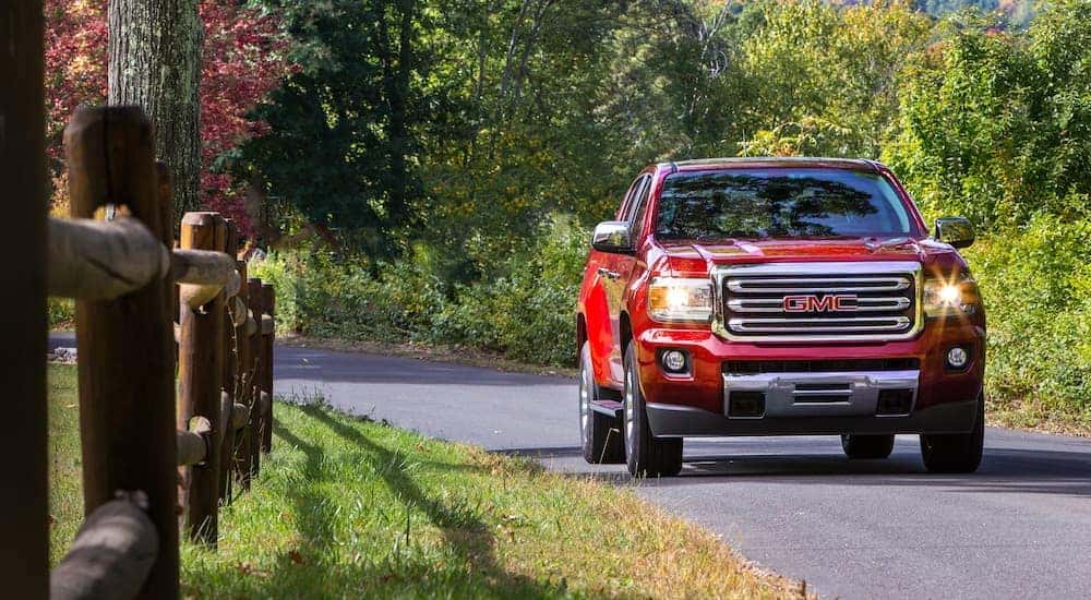 A red 2018 GMC Canyon SLT Diesel is shown driving past a fence.