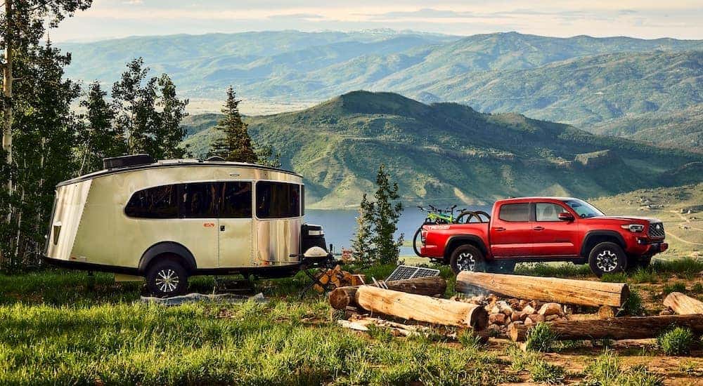 A red 2021 Toyota Tacoma TRD is shown from the side parked at a camp site towing a trailer.
