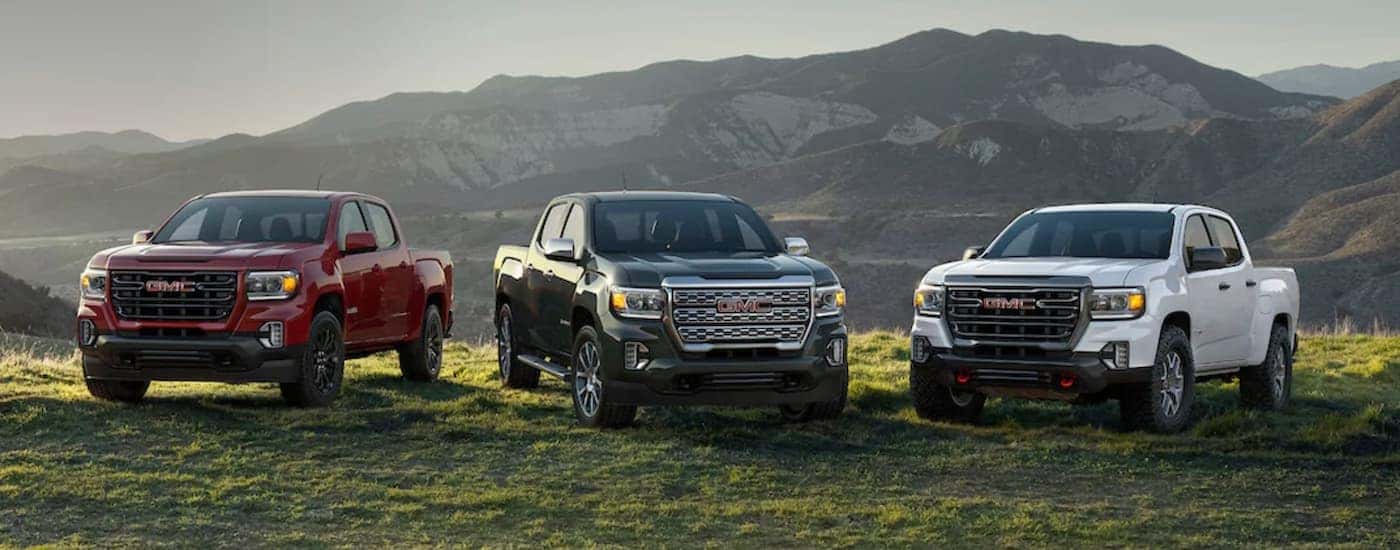 A red, a grey, and a white 2021 GMC canyon are parked on grass in front of mountain.