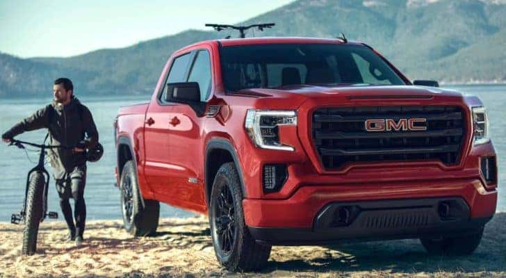 A man with a bike is next to a red 2021 GMC Sierra 1500 at a lake.