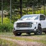 A white 2020 GMC Acadia AT4 is parked in the grass after leaving a used GMC SUV dealer.