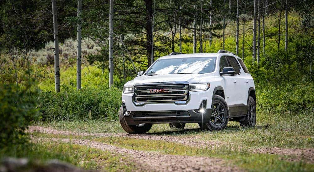 A white 2020 GMC Acadia AT4 is parked in the grass after leaving a used GMC SUV dealer.