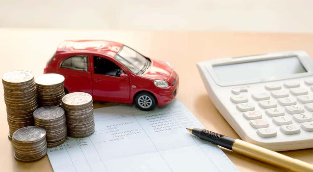 A toy car, calculator, and coins are shown on a desk.