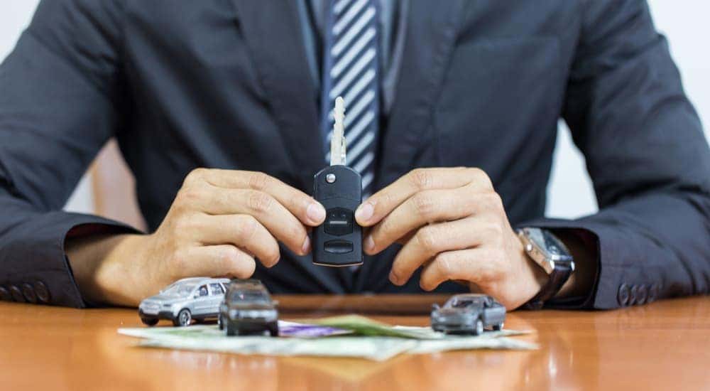 A car salesman is shown holding a car key at a desk.
