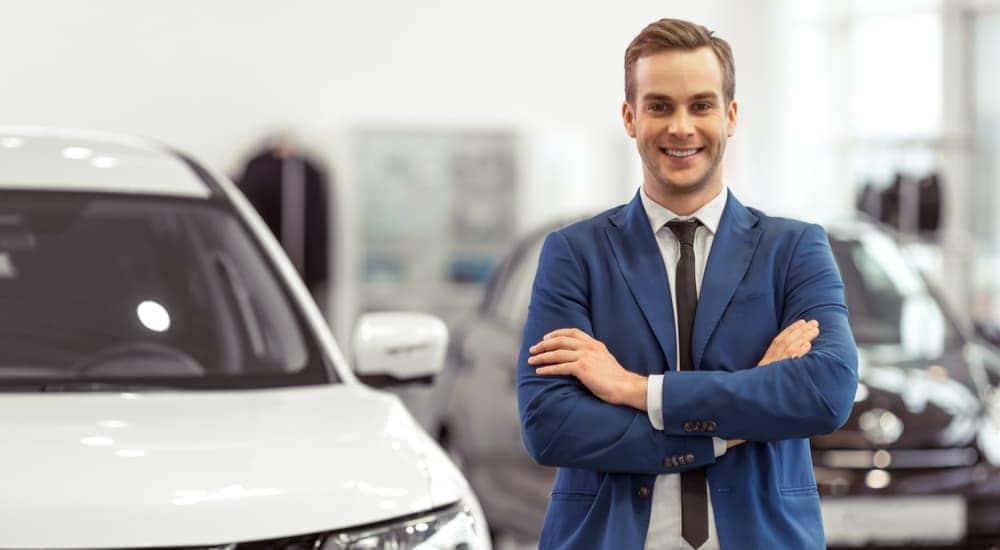 A salesman is shown standing next to a white SUV ready to help you sell your car.