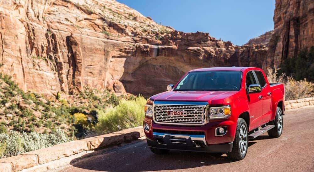 A red 2019 GMC Canyon Denali is shown driving on a road through rocky mountains.