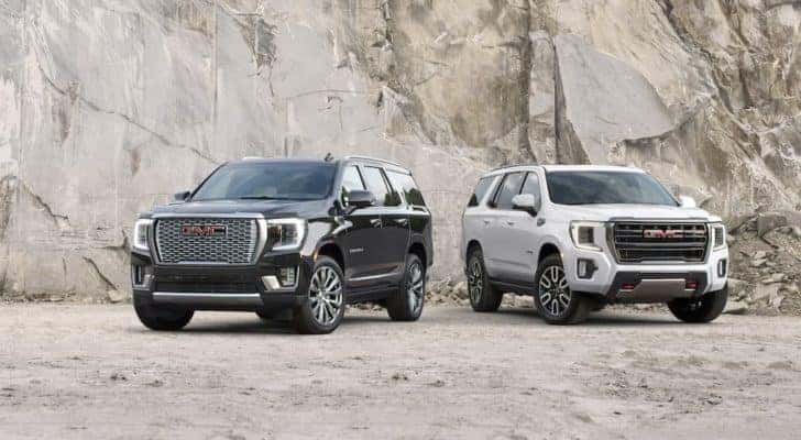A black 2021 GMC Yukon Denali and a white AT4 are shown parked in a quarry.