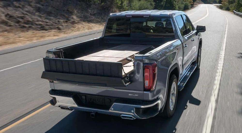 A grey 2022 GMC Sierra Limited is shown from behind driving on a road with lumber in the bed.