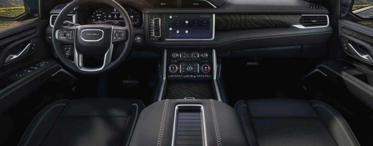 The black interior of a 2022 GMC Yukon shows the steering wheel and infotainment screen.