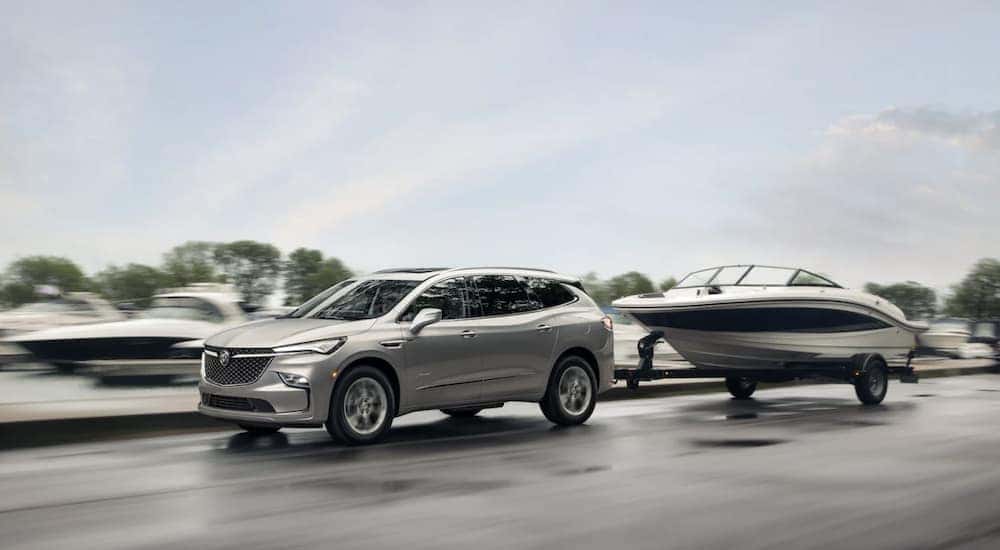 A silver 2022 Buick Enclave is shown from the side towing a boat.
