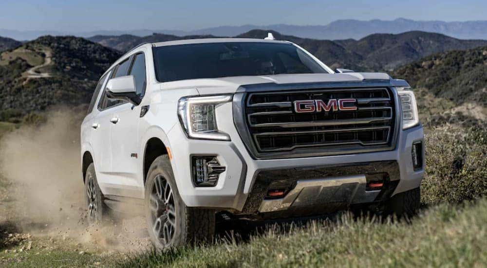 A white 2022 GMC Yukon is shown from the front off-roading through a field.