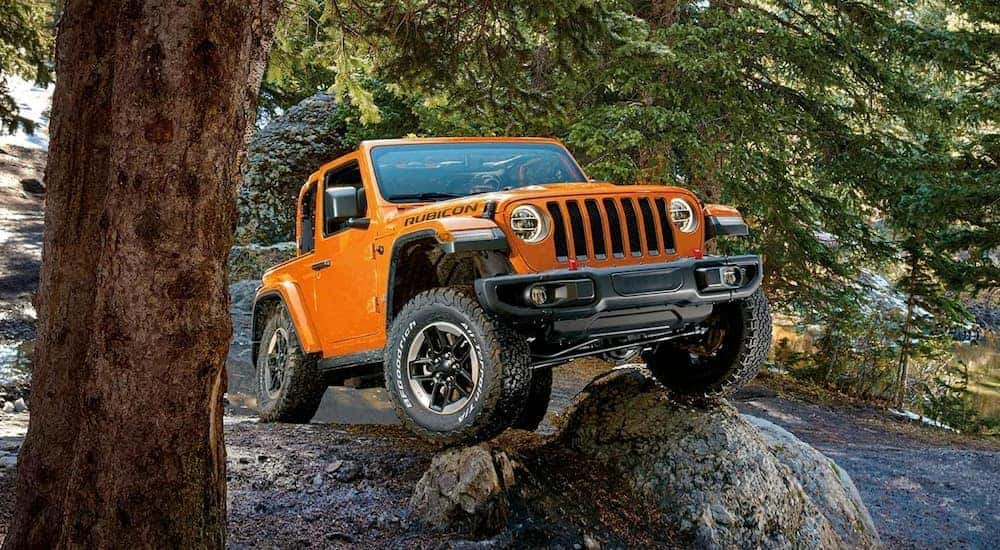 An orange 2019 Jeep Wrangler Rubicon is shown off-roading on a steep rocky trail.