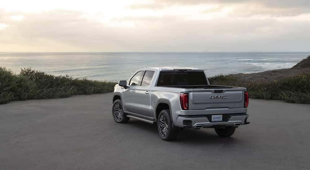 A silver 2022 GMC Sierra 1500 Denali Ultimate is shown from the rear at an angle while parked in a coastal lot.
